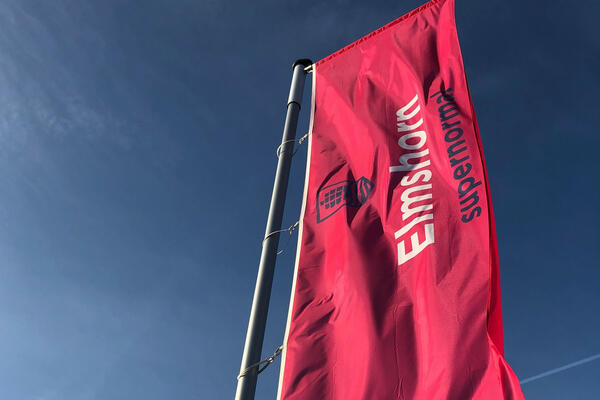 Eine erdbeerrote Flagge mit der Aufschrift "Elmshorn supernormal" weht vor blauem Himmel im Wind.