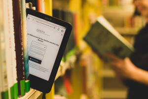 Es zeigt einen E-Book-Reader der aus einem Regal ragt