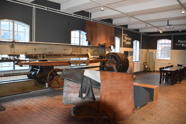 Ausstellungsbereich der Lederindustrie mit einer großen Maschine und Lederhäuten.