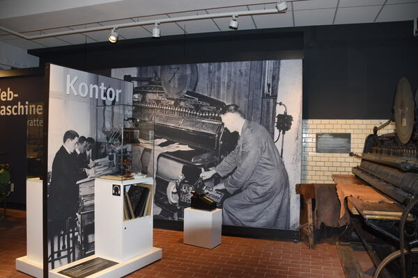 Ausstellungsbereich zum Thema Kontor mit großflächigen Fotos und einer Original-Rechenmschine.