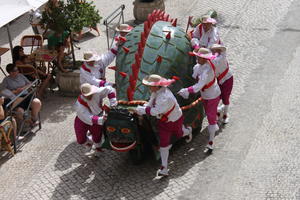 Sieben Männer schieben, bei einem Straßenumzug, eine drachenähnliche Figur (Tarasque) durch Tarascon.