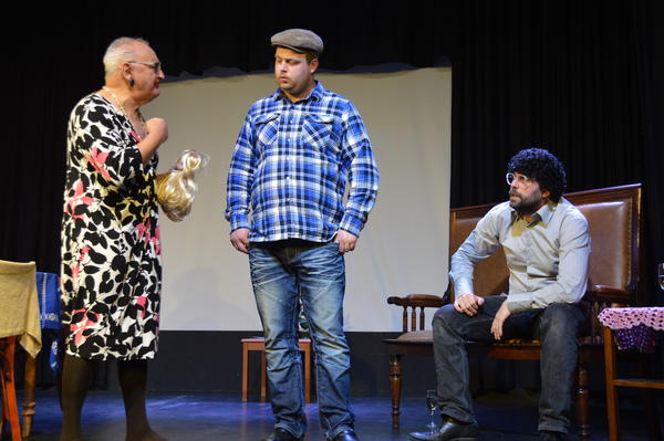 Eine Szene auf der Theaterbühne zeigt drei Akteure im Gespräch.