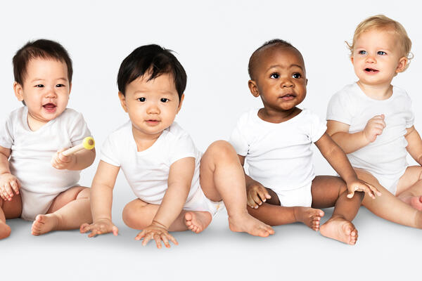 Symbolbild: Mehrere Kleinkinder unterschiedlicher Haut- und Haarfarbe mit weißen Bodys sitzen nebeneinander.