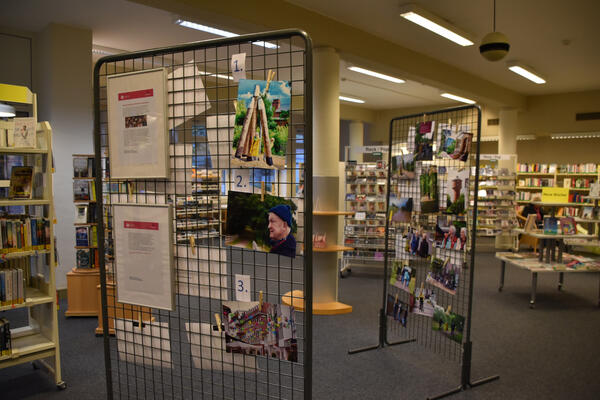 Fotos und Informationstafeln hängen an Gitter-Stellwänden in der Stadtbücherei.